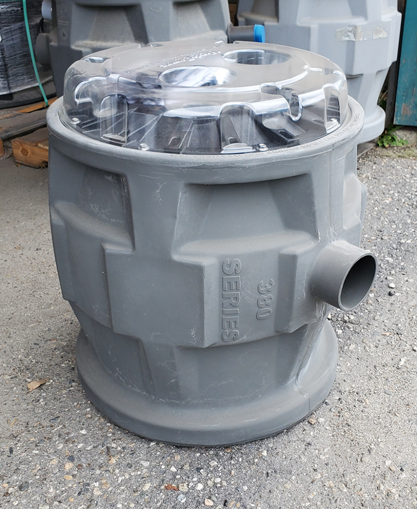 "Image of a plastic sump with a transparent cover and a side outlet pipe, placed on a concrete surface."