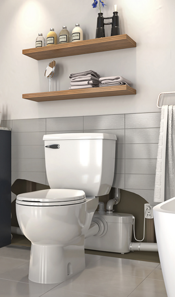 "Image of a bathroom with a toilet and an above-grade sump system installed behind it, along with shelves holding toiletries and towels."