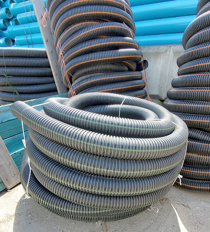 "Photo of a coiled four-inch corrugated perforated polyethylene pipe, stored outdoors alongside similar pipes."
