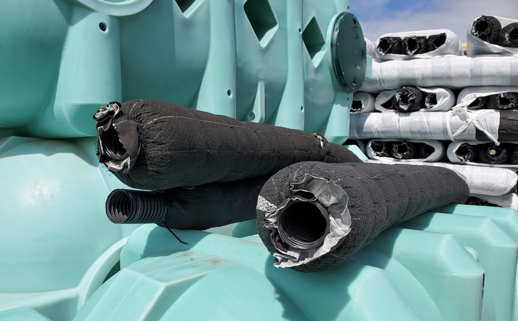 "Photo of corrugated perforated pipes wrapped in fabric, placed on top of large plastic tanks for drainage applications."